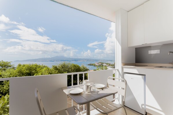 A balcony with a table set for two, overlooking a scenic view of a body of water and distant land.