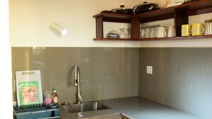 Una cocina con un lavamanos de acero inoxidable, un escurreplatos y una repisa superior con diversos utensilios de cocina.
