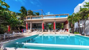 A pool area with lounge chairs and umbrellas, a bar, and a building with a balcony.