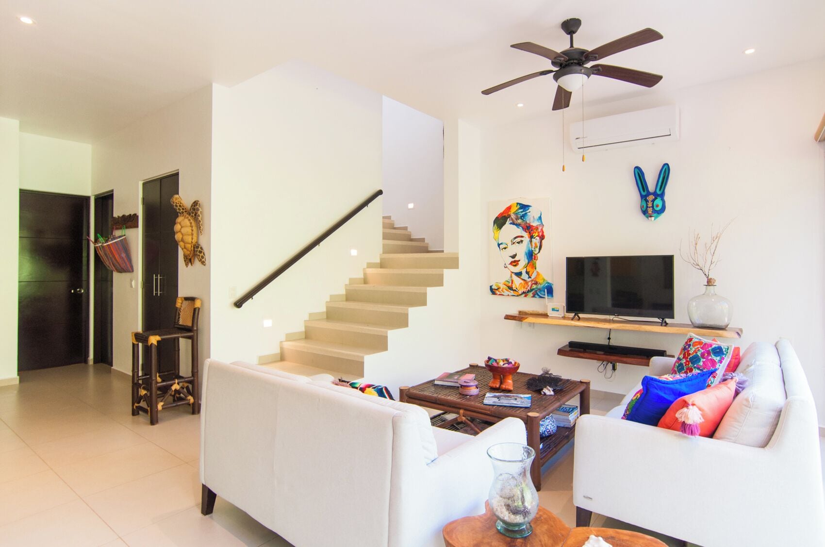 Una sala de estar moderna con una escalera, un televisor de pantalla plana y un ventilador de techo.