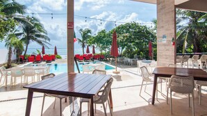 A poolside area with tables and chairs, a pool, and a view of the ocean.