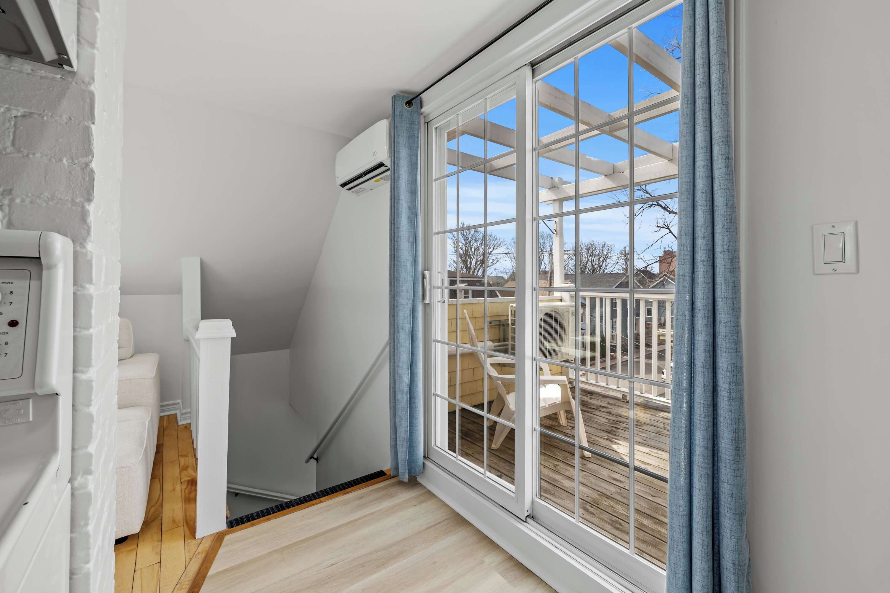 A room with a wooden floor, a white wall, a window with blue curtains, and a white ceiling.