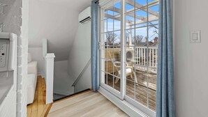 Una habitació amb sòl de fusta, paret blanca, finestra amb cortines blaves i sostre blanc.