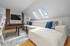 A modern living room with a sofa, a TV, a coffee table, and a skylight.