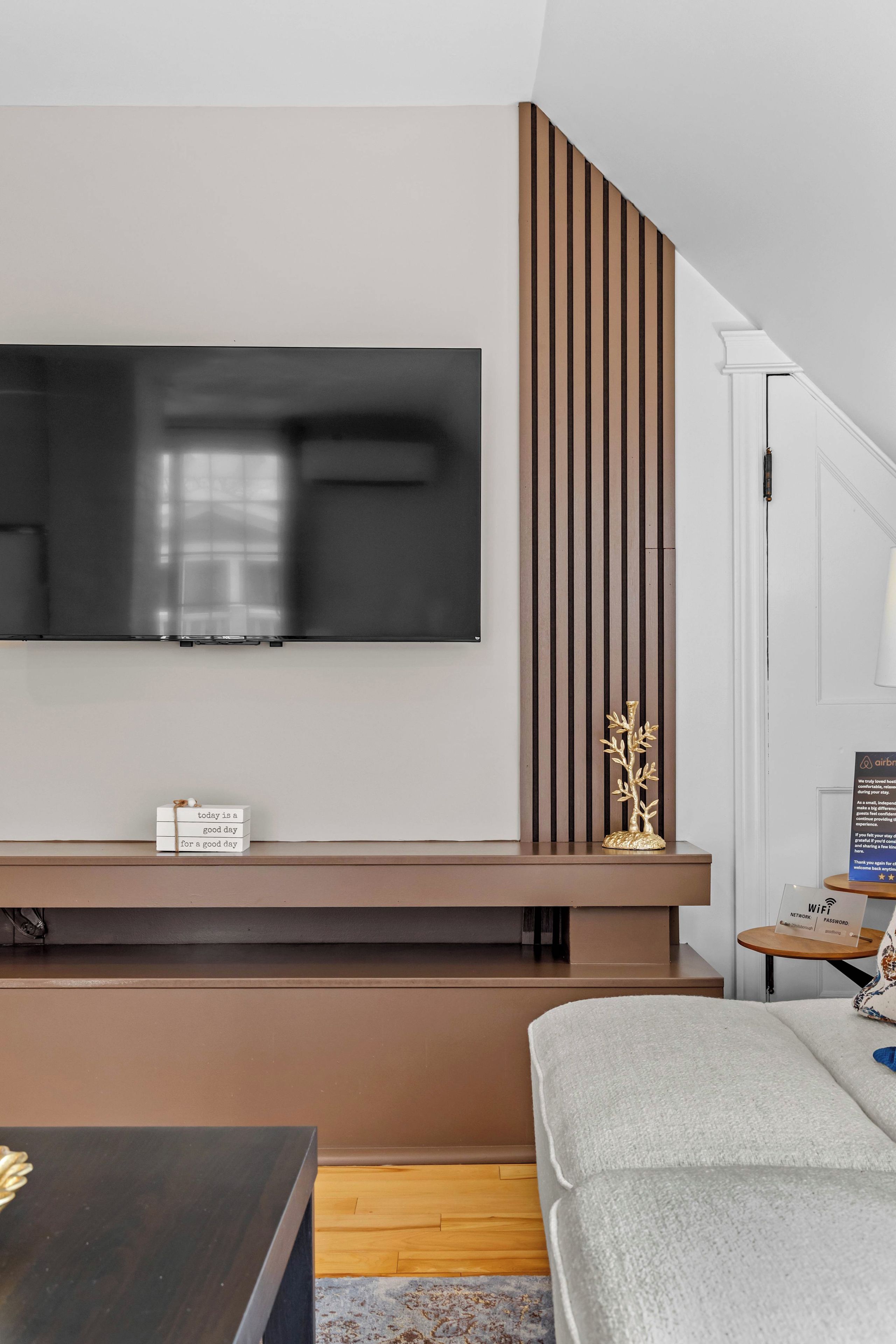 Un salon moderne avec un téléviseur à écran plat fixé au mur, un mur d’accent en bois, une petite table avec un panneau et un canapé.