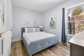 A bedroom with a bed, a radiator, a window with curtains, and artwork on the walls. - Heritage Harbour 2 Bed 2 Bath Close to Waterfront (Charlottetown)