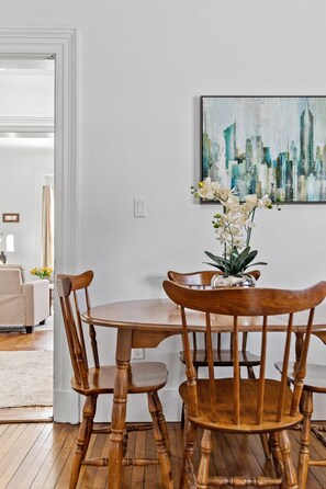 A dining area with a wooden table and chairs, a vase with white flowers, and a cityscape painting on the wall. - Spacious Downtown Retreat at Ole King Square (Charlottetown)