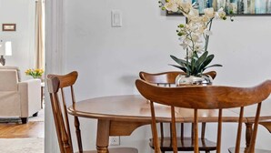 Un comedor con mesa y sillas de madera, un florero con flores y un cuadro de la ciudad en la pared.