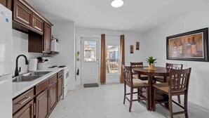 A modern kitchen with brown cabinets, white countertops, and a dining area with wooden chairs and a table. - Downtown Urban Comfort Spacious 1 Bdrm Apartment (Charlottetown)