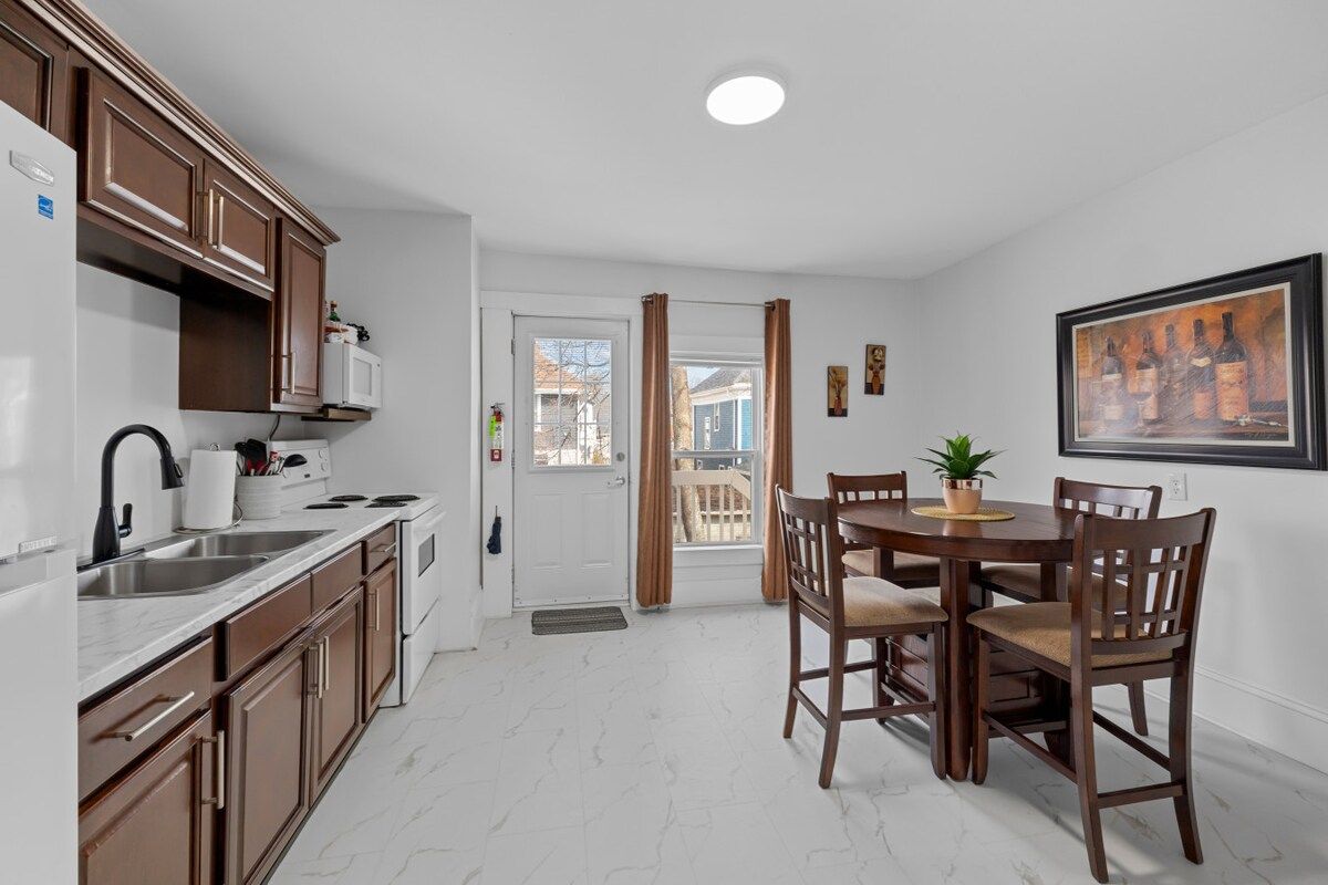 Cozinha compacta com área de refeições, piso de mármore branco e vista pela porta.