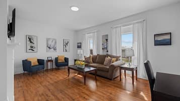 A modern living room with hardwood flooring, a brown sofa, two armchairs, a coffee table, and a TV.