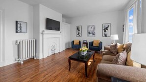 A modern living room with hardwood flooring, a fireplace, a flat-screen TV, and a sofa set. - Downtown Urban Comfort Spacious 1 Bdrm Apartment (Charlottetown)