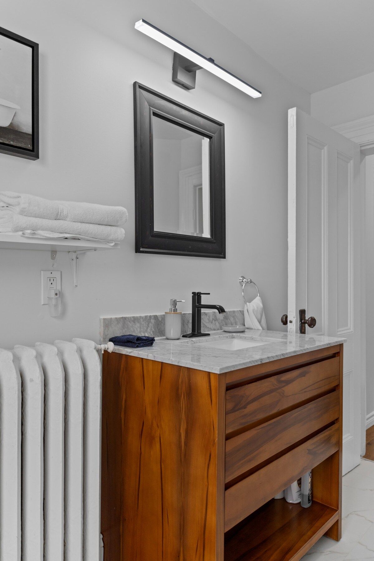 A modern bathroom with a wooden vanity, a mirror, a towel rack, and a built-in heater.