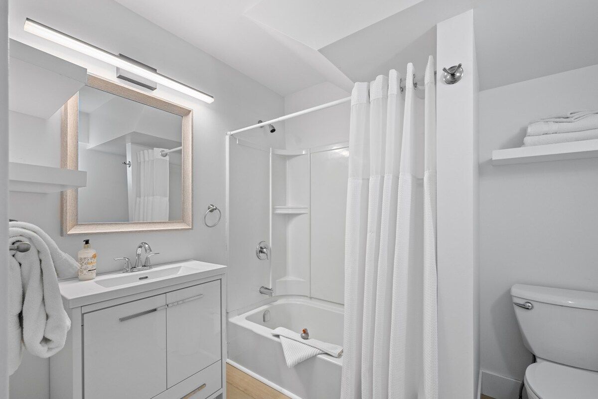 Une salle de bain moderne avec un meuble-lavabo blanc, un grand miroir, une baignoire et des toilettes.