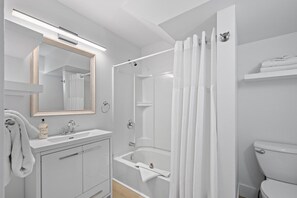 Une salle de bain moderne avec un meuble-lavabo blanc, un grand miroir, une baignoire et des toilettes.