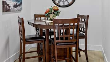 A dining area with a round table, four wooden chairs, a wall clock, and a painting of a lighthouse.