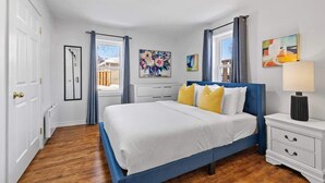 Une chambre à coucher avec un grand lit, une table de chevet, une commode et une fenêtre avec des rideaux.