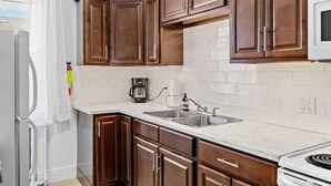 Une cuisine avec des meubles de rangement en bois, un plan de travail blanc, un évier, une cuisinière et un four à micro-ondes.