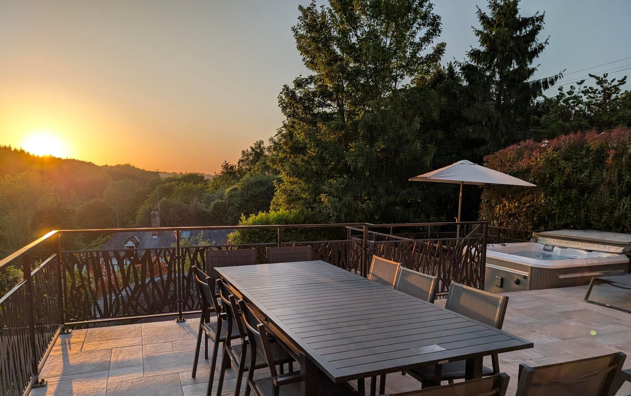 An outdoor patio with a table and chairs, a barbecue grill, and a view of the sunset.