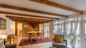 Ein Essbereich mit Holzbalkendecke, einem für vier Personen gedeckten Tisch und Blick ins Freie durch große Fenster.