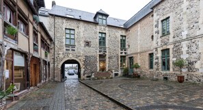 A courtyard with cobblestone pavement, stone buildings, and a central archway.