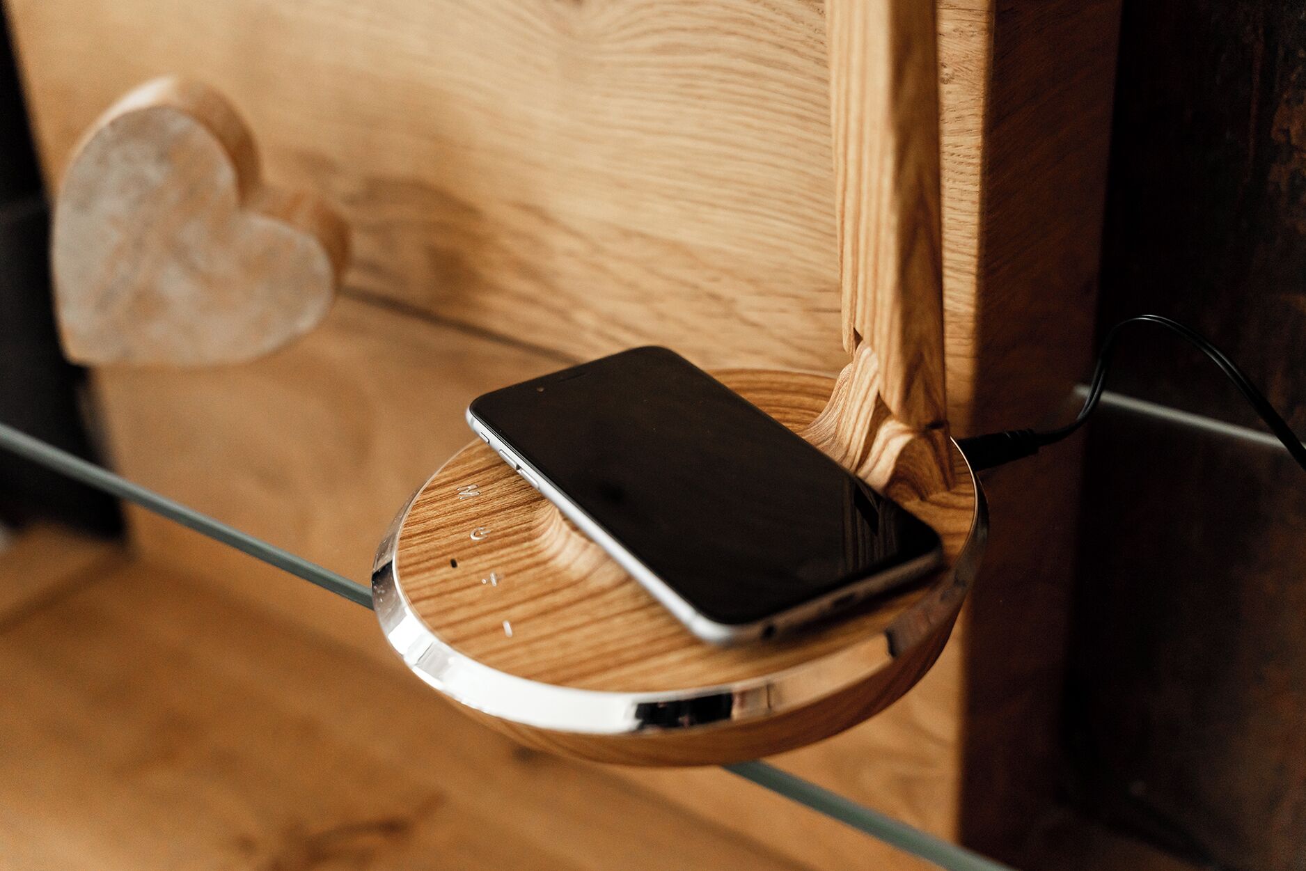A smartphone on a wooden charging dock attached to a glass table.