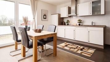 A modern kitchen with white cabinets, a wooden dining table, and a view through the window.