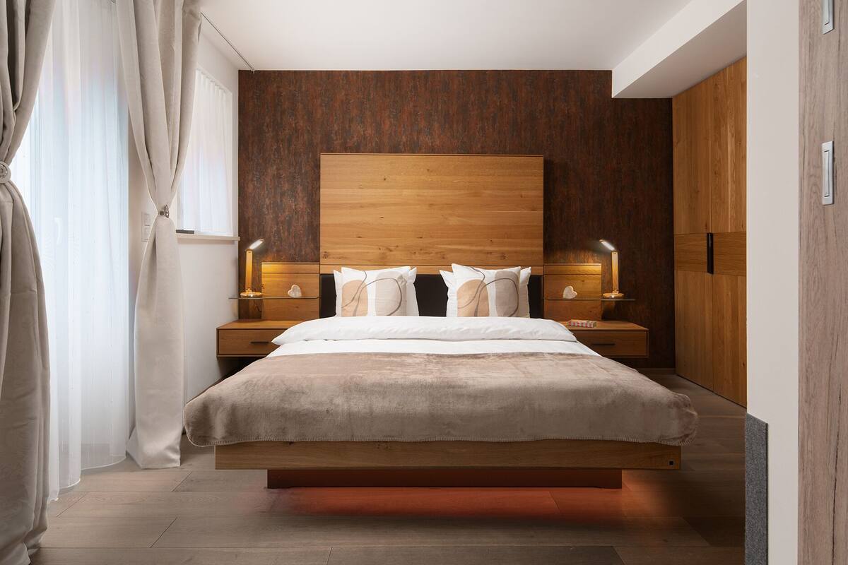 Une chambre moderne avec une tête de lit en bois, un lit avec une literie blanche, deux tables de chevet avec des lampes et une armoire en bois.