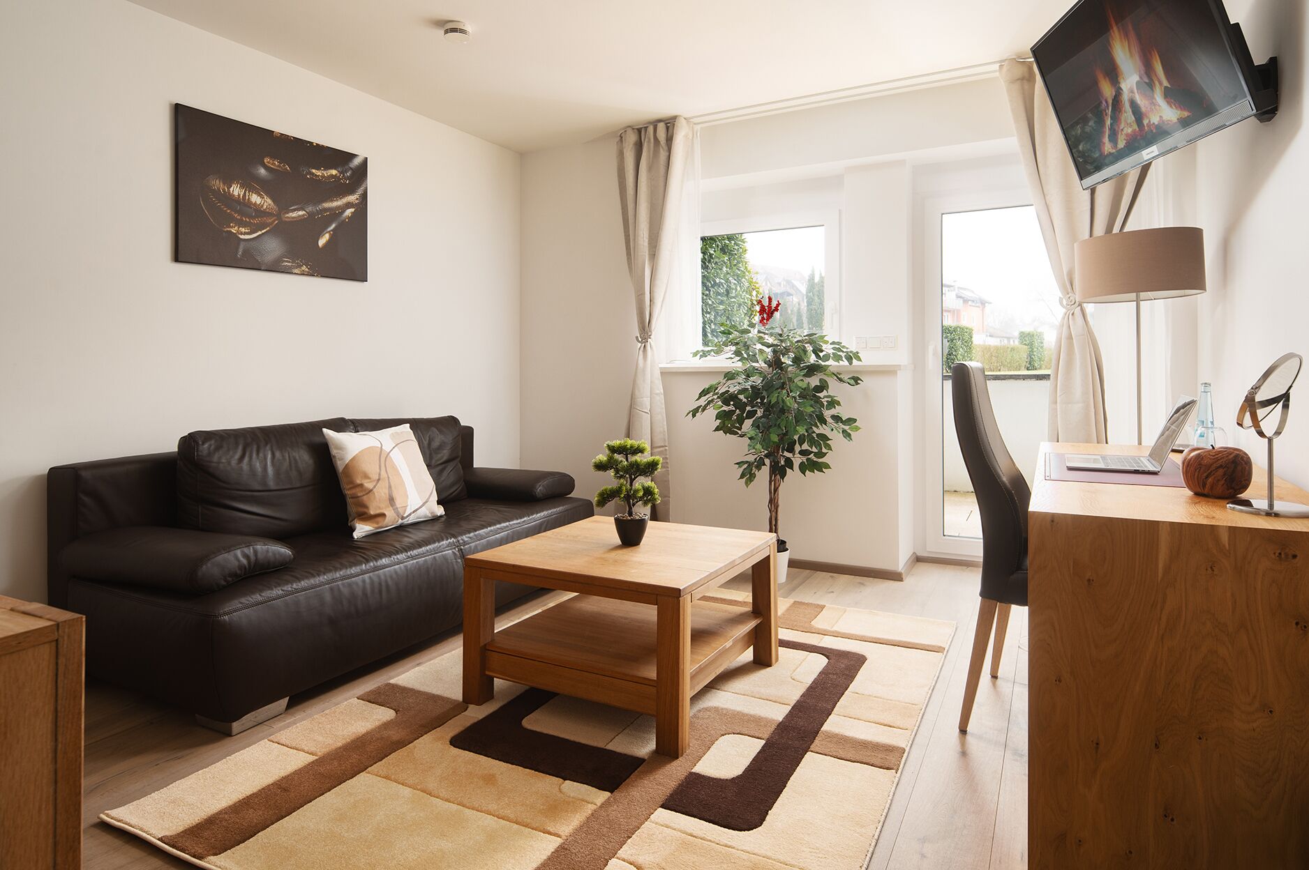 A modern living room with a leather sofa, a wooden coffee table, a potted plant, and a desk with a laptop.