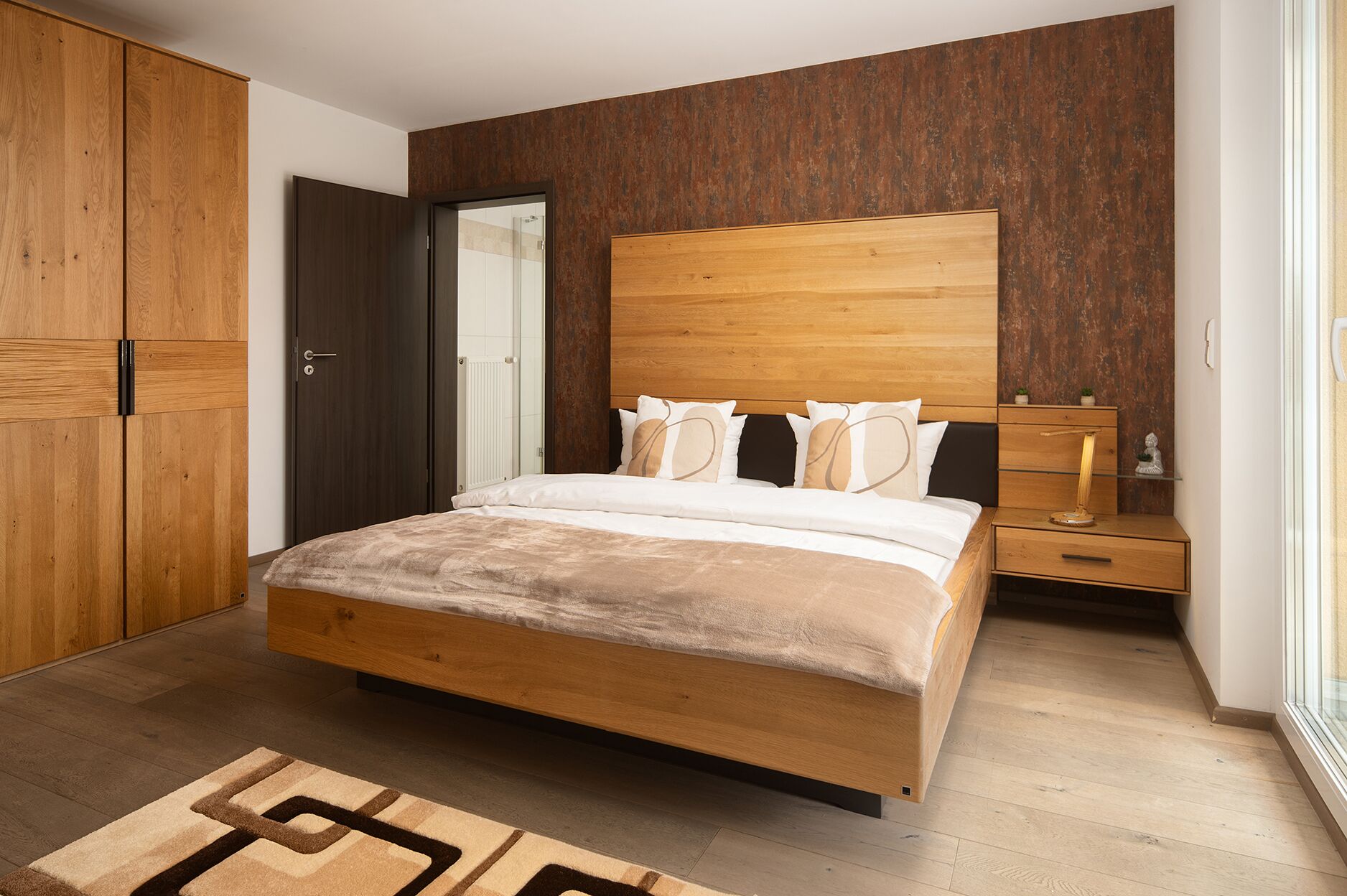 A bedroom with a wooden bed, a nightstand, a wardrobe, and a bathroom visible through an open door.