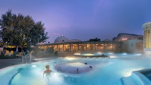 Een verwarmd buitenzwembad met ligbedden en een gebouw op de achtergrond.