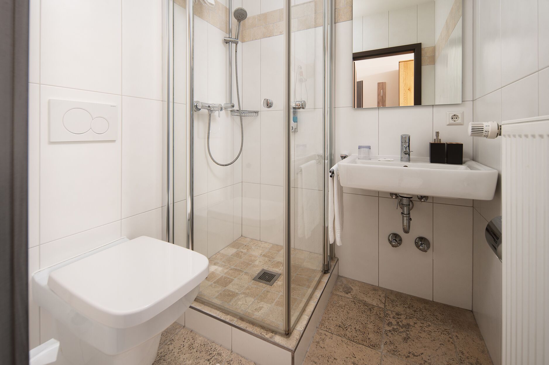 Een moderne badkamer met een douchecabine van glas, een wit toilet en een wastafel met een spiegel erboven.