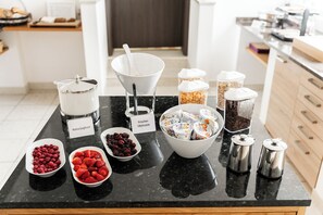 Ein Frühstücksbuffet mit beschrifteten Behältern für Joghurt, Müsli und Früchte wie Himbeeren und Erdbeeren.