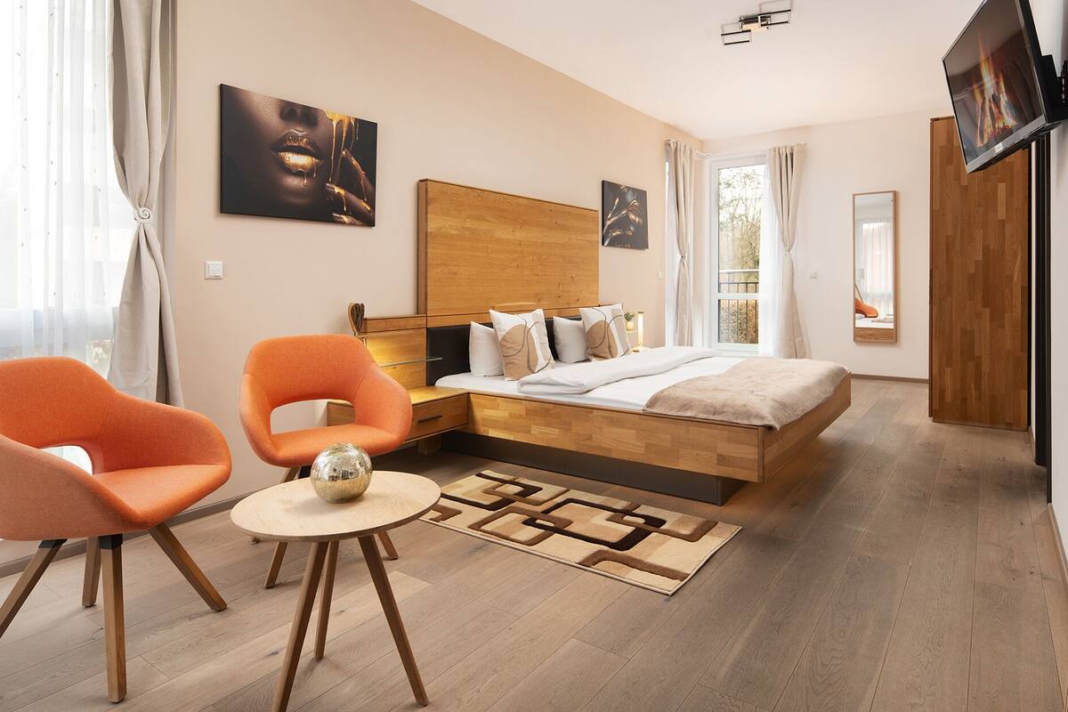 Une chambre à coucher moderne avec un lit en bois, un fauteuil orange et une petite table ronde sur laquelle est posé un bol décoratif.