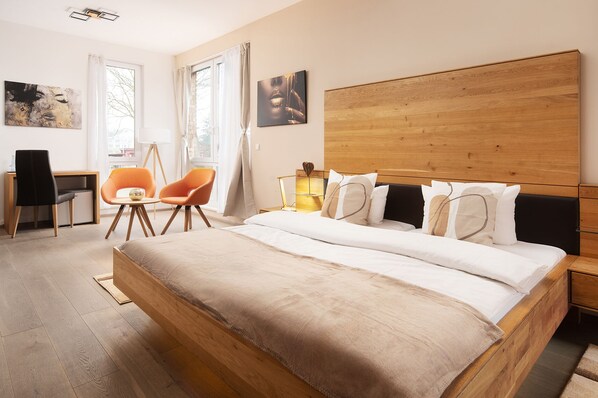 A modern bedroom with a wooden bed, a desk, two chairs, and artwork on the walls.