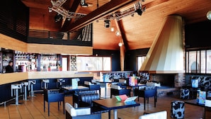 Ein Restaurant mit hohen Holzbalkendecken, einer Bar und verschiedenen Sitzgelegenheiten, darunter Boxen und Tische.