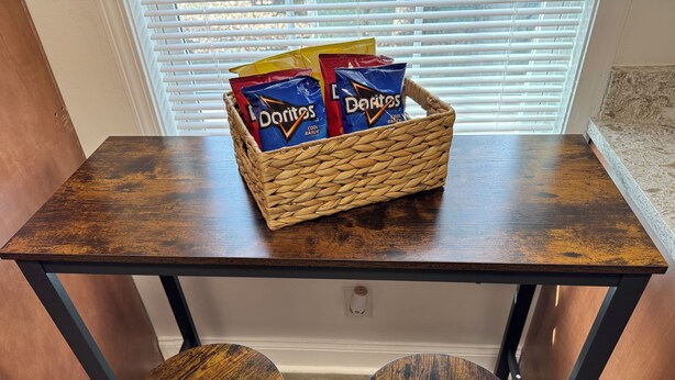 A small dining area with a wooden table and two stools. A woven basket containing bags of Doritos chips is placed on the table. - Newly Renovated near everything in Downtown Atlanta and Mercedes Stadium.  (Atlanta)