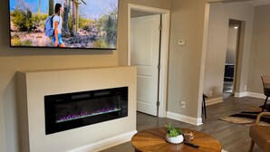 A living room with a flat-screen TV mounted above a fireplace, a ceiling fan, and a round wooden coffee table with a plant. - Newly Renovated near everything in Downtown Atlanta and Mercedes Stadium.  (Atlanta)