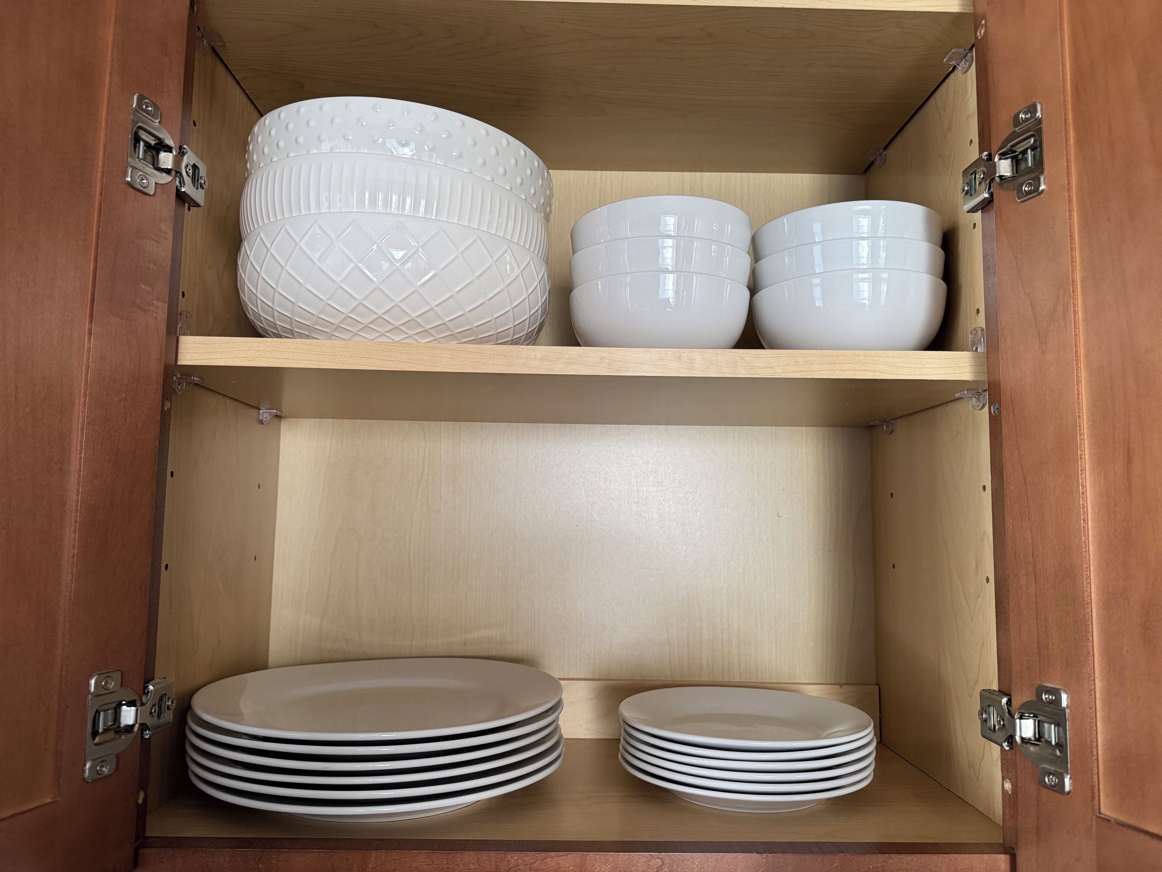A wooden cabinet with three shelves, each holding white bowls and plates.