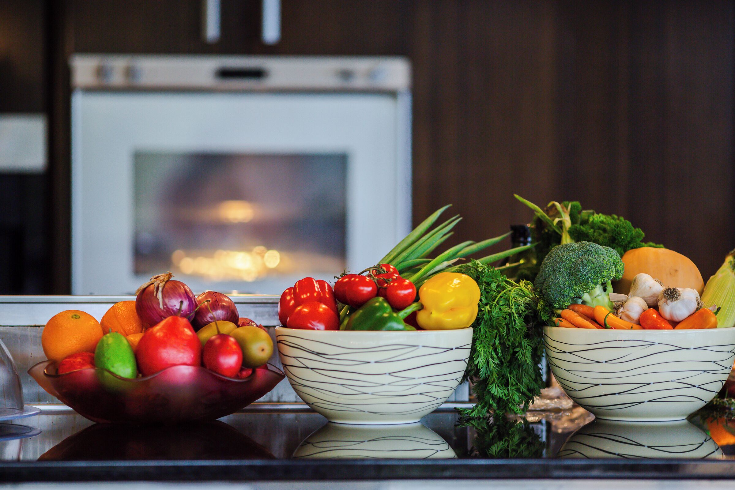 Two bowls of assorted vegetables on a kitchen counter with a stove in the background.