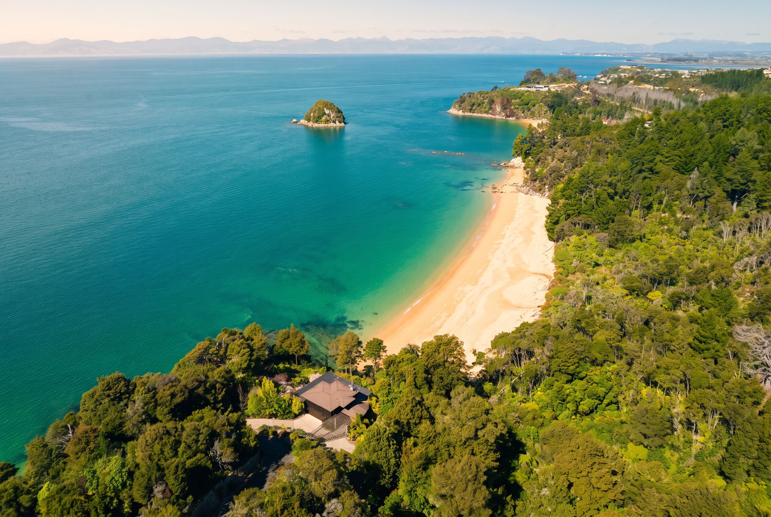 An aerial view of a coastal property with a beach, forested area, and a small island.