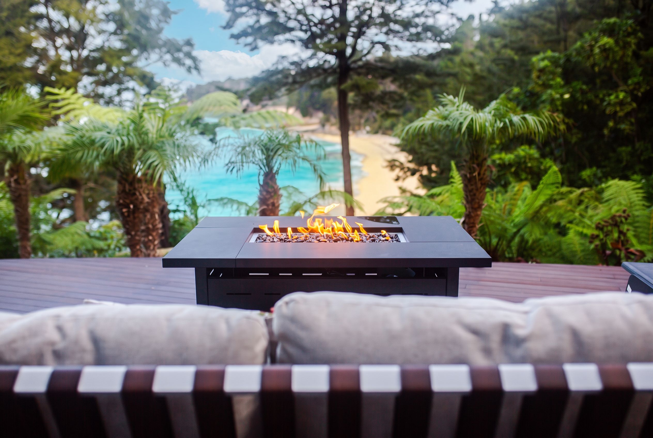 A fire pit on a deck with a view of a beach and palm trees.