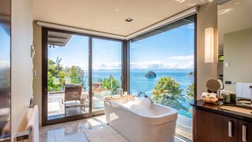 Un bagno moderno con una vasca da bagno ampia, una doccia vetrata e vista sul mare.