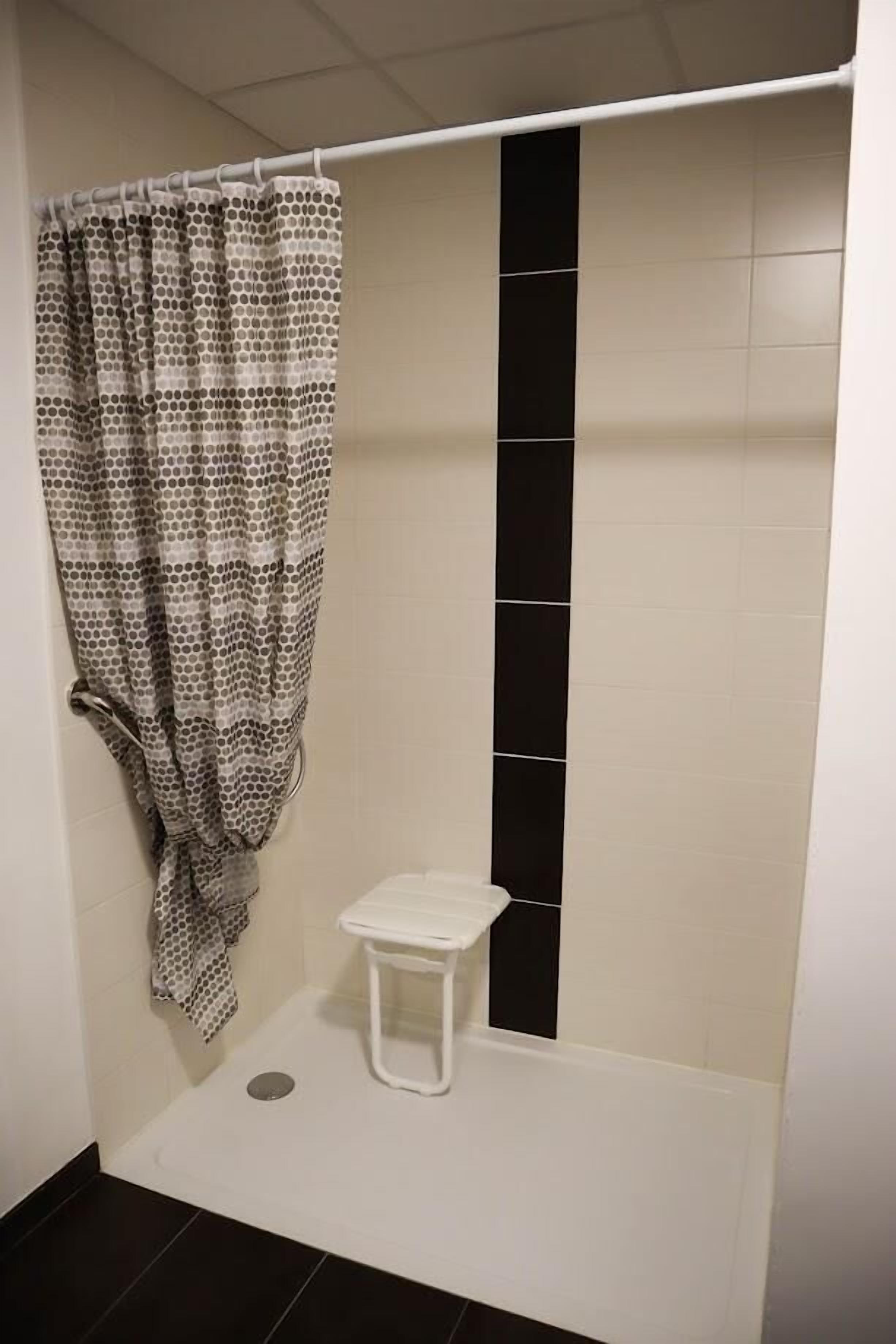 Un baño pequeño con cortina de ducha, un lavamanos blanco y un detalle de baldosas verticales negras.