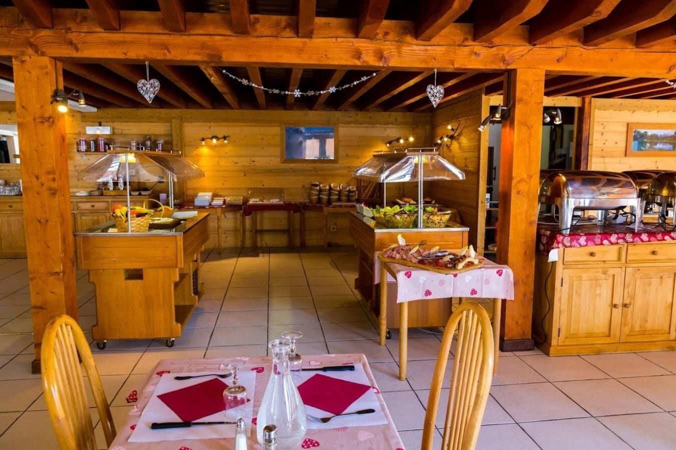 A cozy restaurant with wooden interiors, a buffet counter, and a dining area with tables set for two.