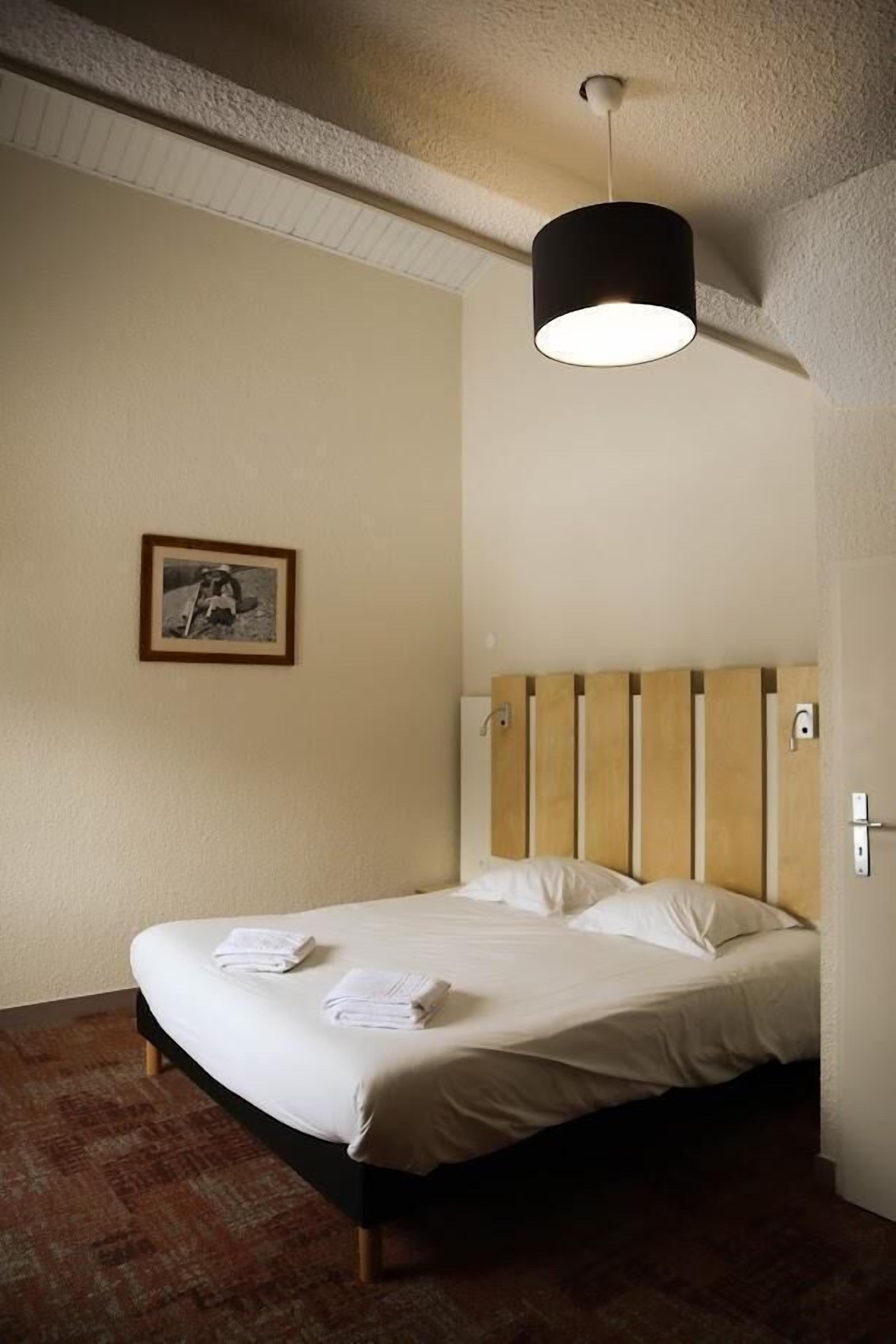 A hotel room with a single bed, a framed picture on the wall, and a hanging light fixture.