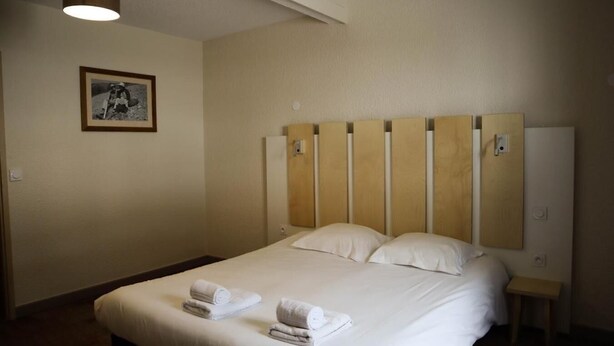 Ein Hotelzimmer mit einem großen Bett, einem Holzkopfende, zwei Kissen, einem Nachttisch, einem kleinen Tisch, einem gerahmten Bild an der Wand und einer Deckenleuchte.