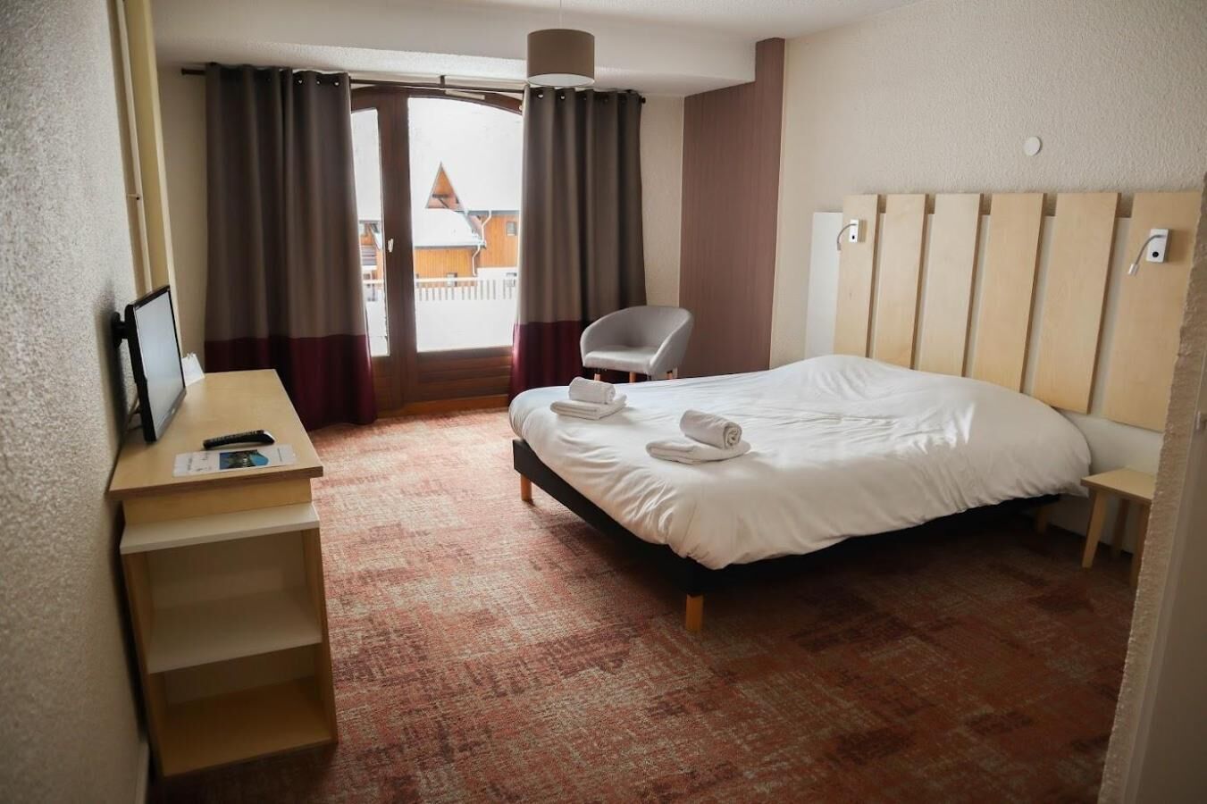 Habitación de hotel con cama, escritorio, silla y vistas al exterior.