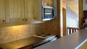 Een keuken met houten kastjes, een inbouwoven en een betegelde achterwand.