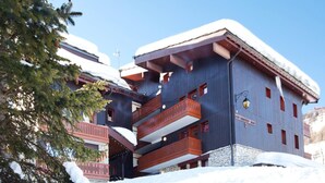 Een meerhoog gebouw met balkons, sneeuw bedekte daken en een stenen basis.